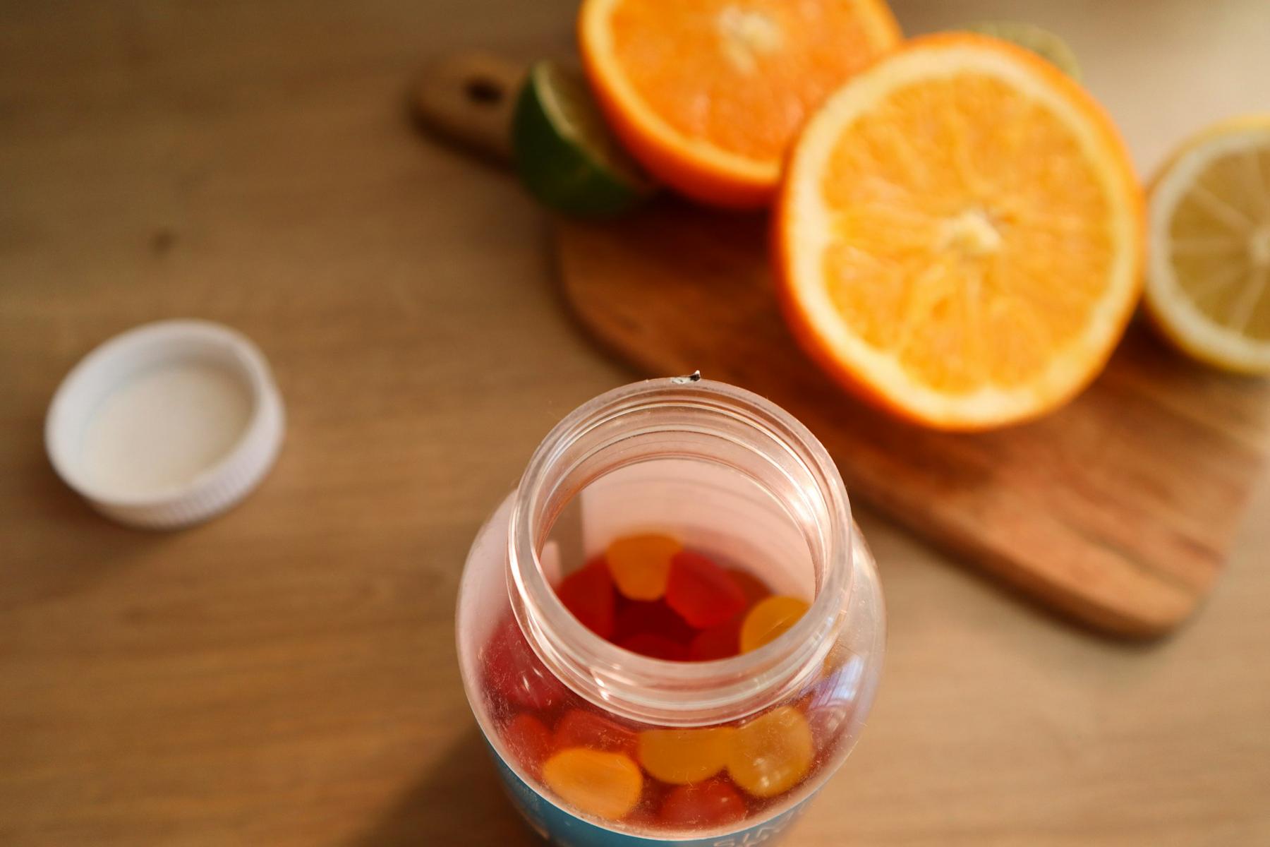 Gummy supplements in a jar next to sliced oranges