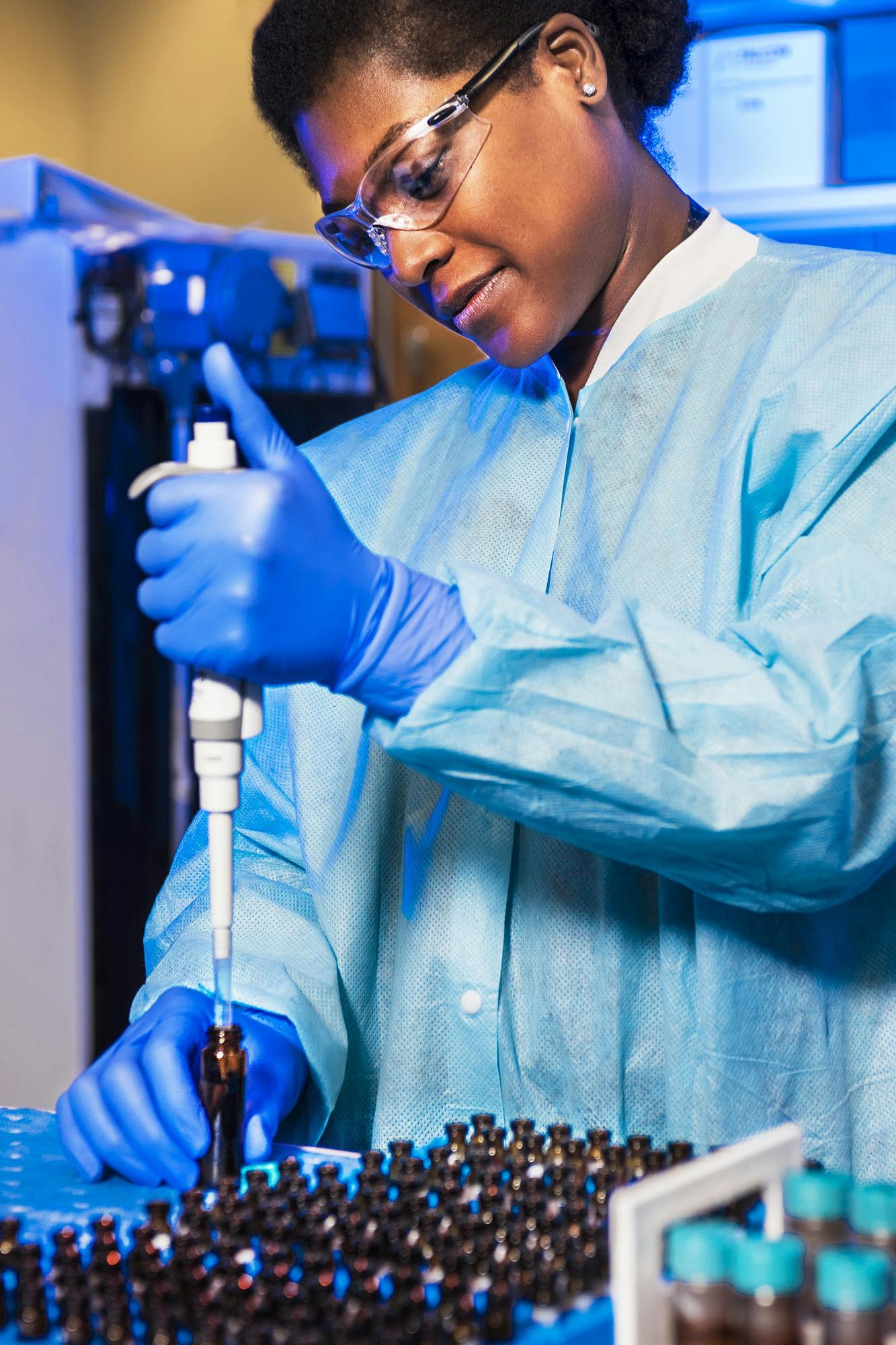 Scientist in a blue gown using a pipette